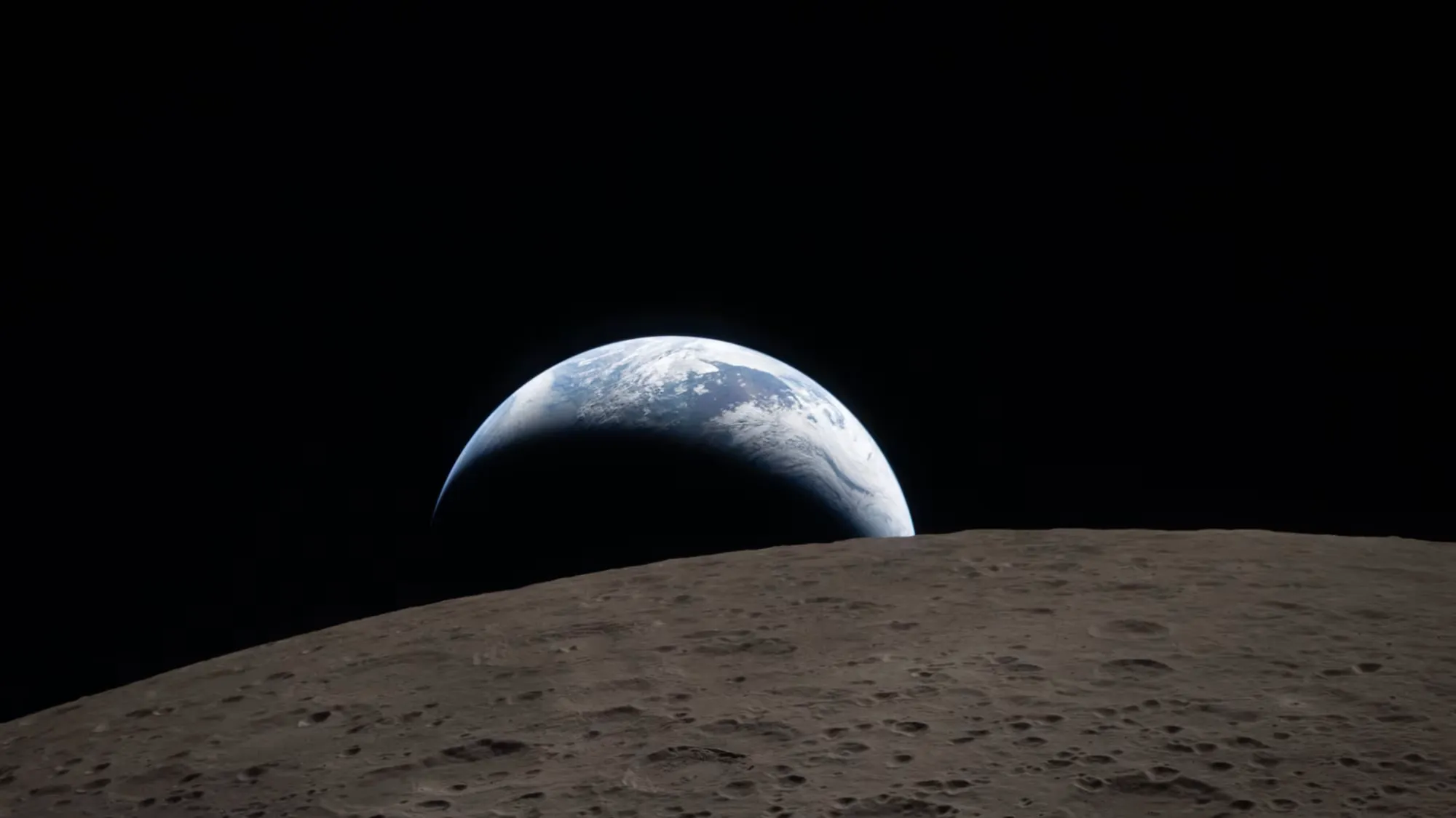 A crescent Earth rising over the gray surface of the Moon